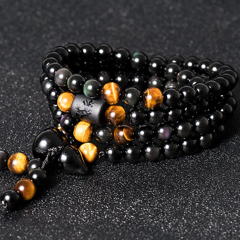 108 bead obsidian tiger eye meditation bracelet coiled 3 layers on dark surface showing engraved cylinder bead and gold accent