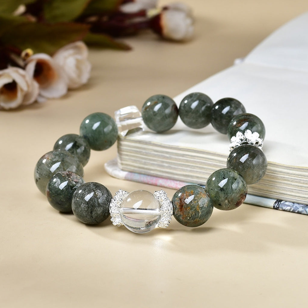 Career advancement energy bracelet with green crystal and clear quartz beads displayed beside a book