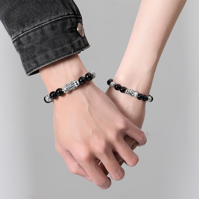 Two people wearing matching black obsidian Pixiu wealth and protection bracelets with silver guardian charms.
