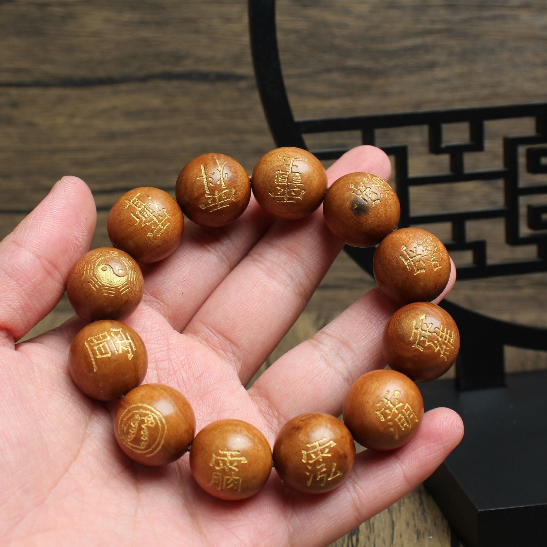 Close-up of a hand holding a thunderstruck wood bracelet engraved with Five Thunders talisman symbols and a Tai Chi bead
