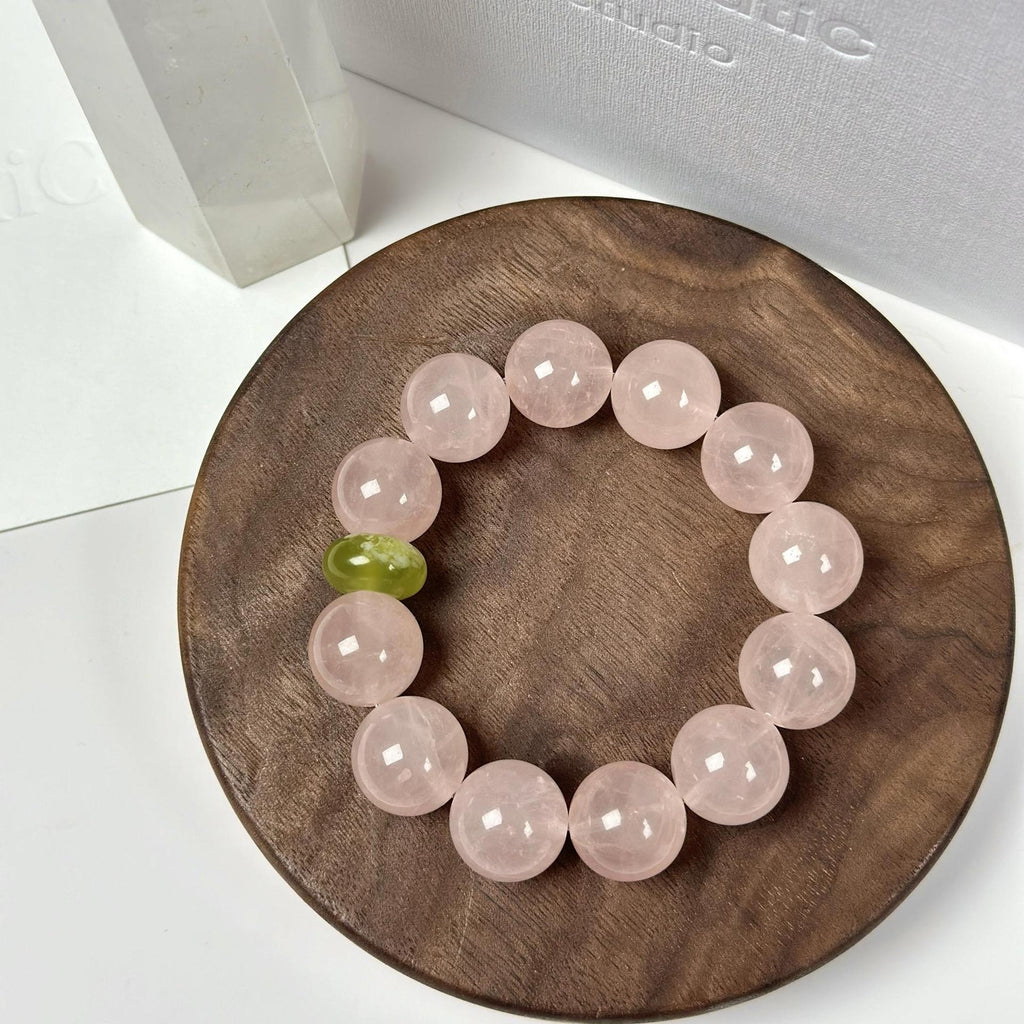 Heart healing crystal bracelet for women with pale pink beads and a green accent bead on a wooden tray