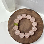 Heart healing crystal bracelet for women with pale pink beads and a green accent bead on a wooden tray