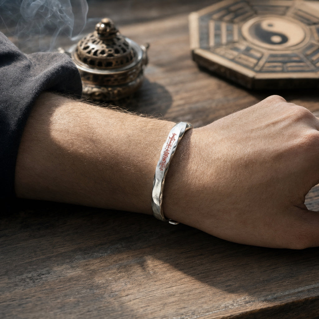 Male wrist wearing a hand-forged 925 silver Taoist Mobius protection bracelet with red cinnabar talisman engraving.