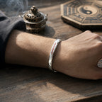 Male wrist wearing a hand-forged 925 silver Taoist Mobius protection bracelet with red cinnabar talisman engraving.