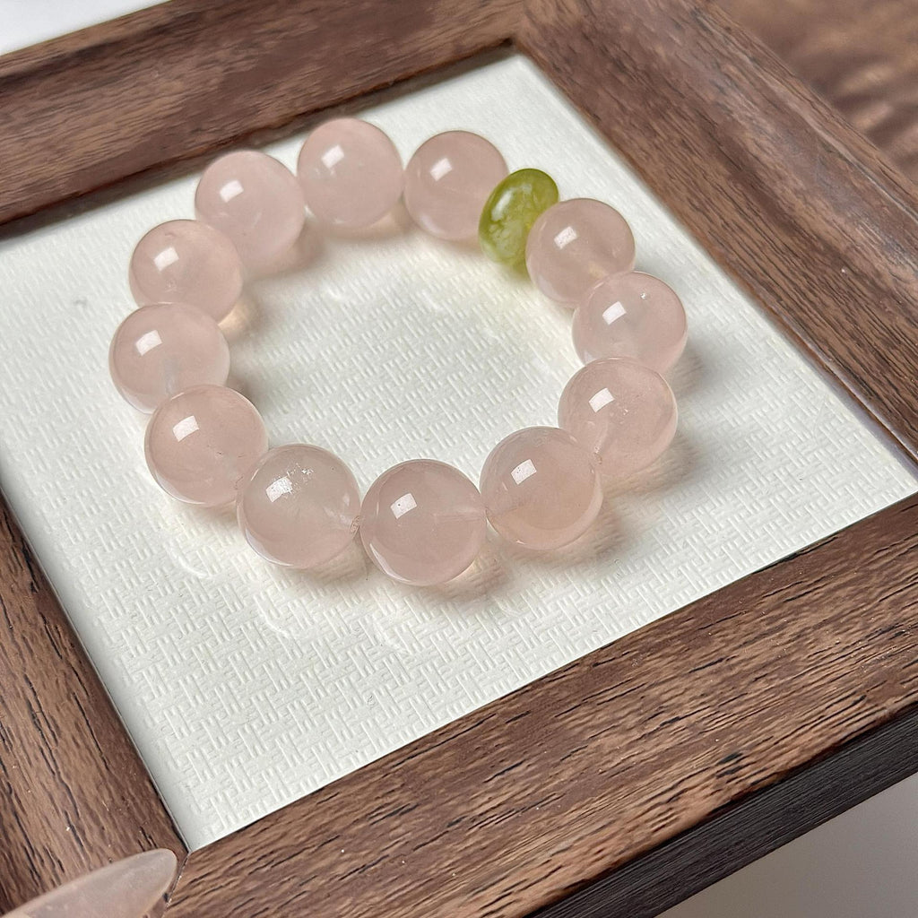 Close-up of a heart healing bracelet with pale pink crystal beads and one green accent bead in a wooden display box