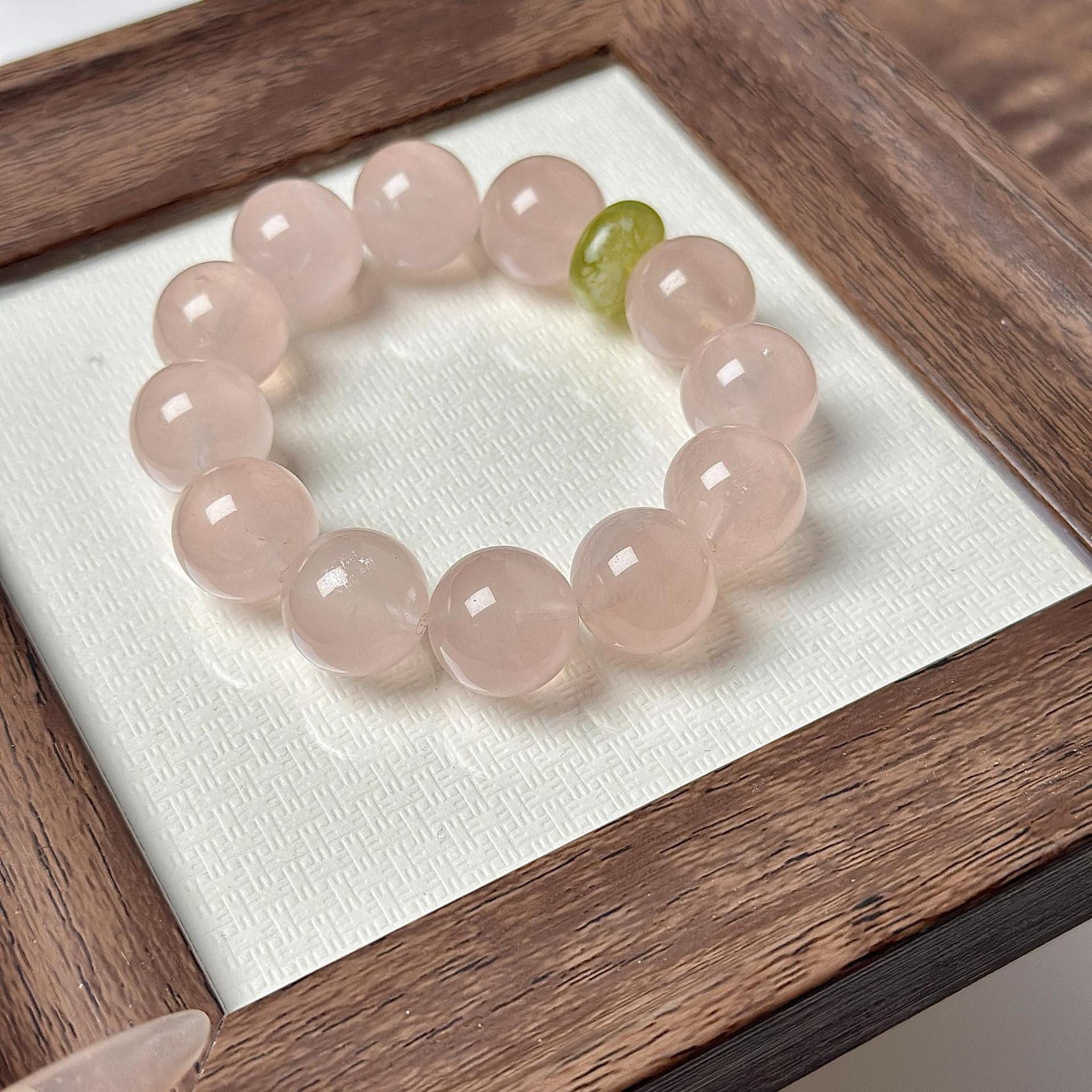 Close-up of a heart healing bracelet with pale pink crystal beads and one green accent bead in a wooden display box