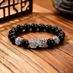 Black obsidian Pixiu bracelet featuring a silver wealth guardian, polished beads, and decorative silver spacers.