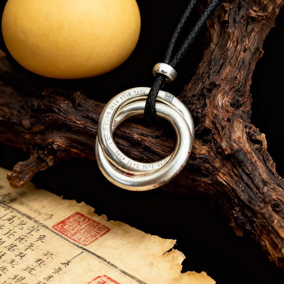 Close-up of a sterling silver Taoist Qiankun circle pendant with circular engravings and black cord beside Daoist ritual objects.