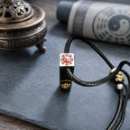 End detail of a Taoist supreme talisman pendant showing a Bagua Yin-Yang symbol, cinnabar detail, and black cord.