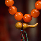 Close-up of the wealth-gathering gourd pendant, South Red Agate beads, green jade accent bead, and five-element tassel on a Taoist wealth bracelet