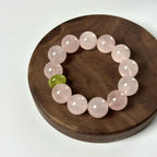 Full view of a women’s heart healing crystal bracelet with pale pink beads and a green accent bead on a wooden tray