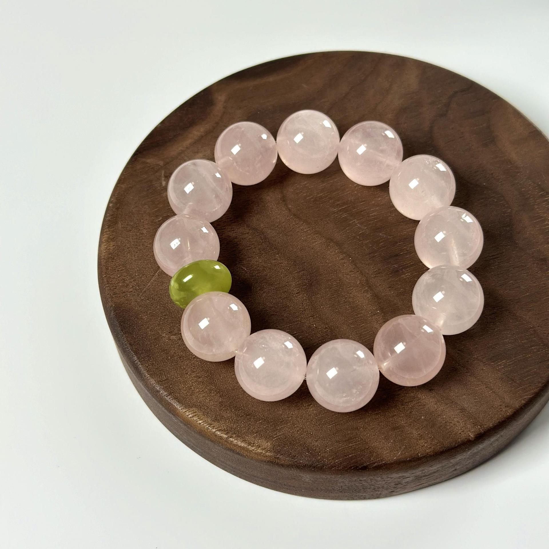 Full view of a women’s heart healing crystal bracelet with pale pink beads and a green accent bead on a wooden tray