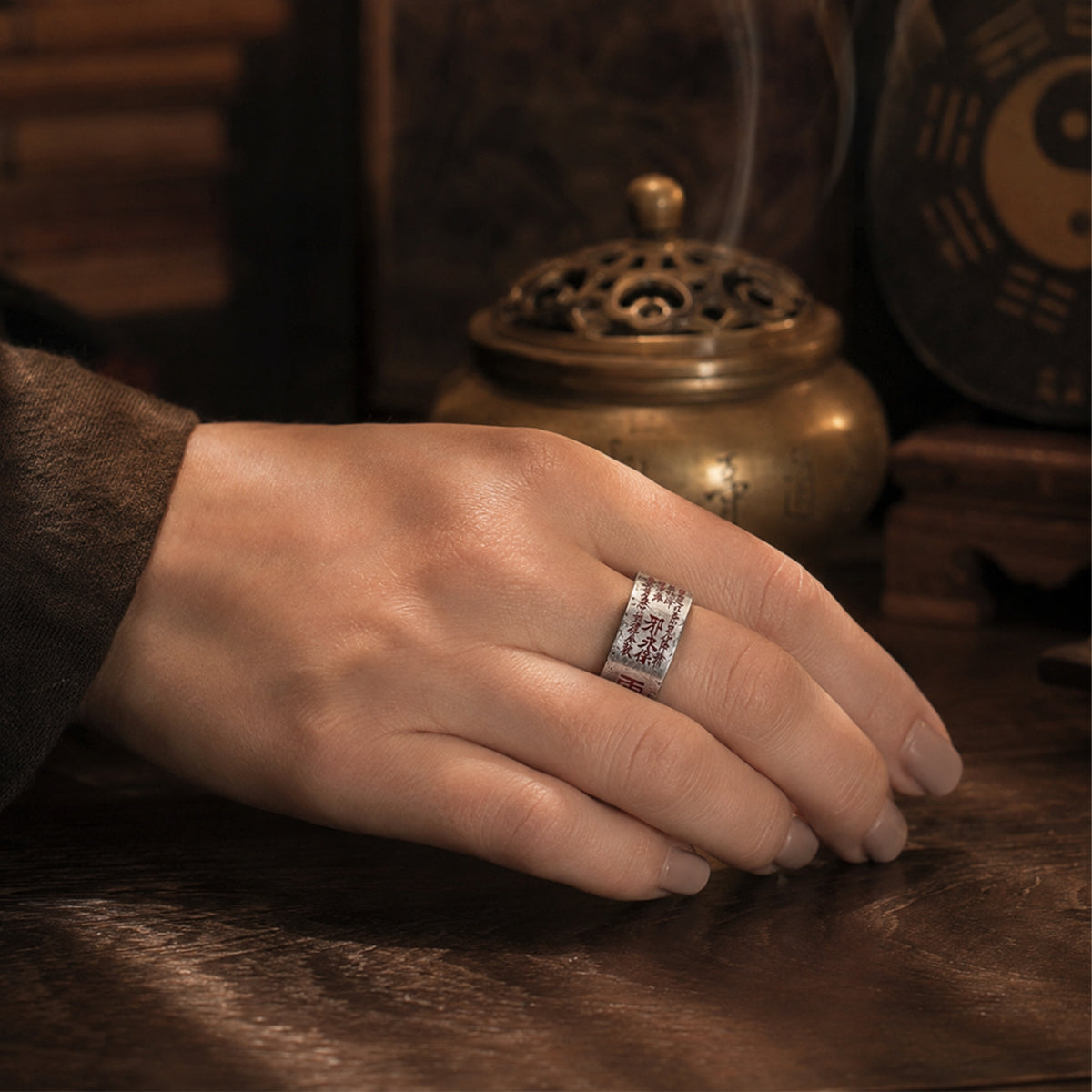 Female hand wearing a Taoist Mountain Ghost Five Thunder protection ring with cinnabar talisman details.