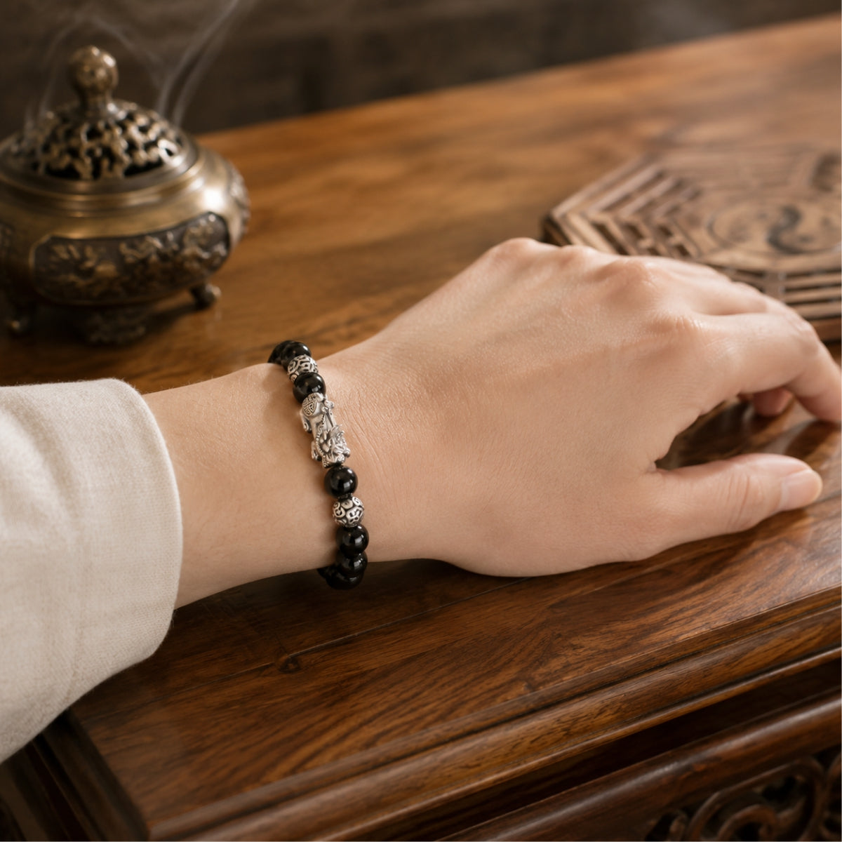 Female wrist wearing a black obsidian Pixiu wealth and protection bracelet with a silver Pixiu charm.