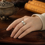 Female hand wearing a Taoist four-talisman protection ring with concealed inner engravings in a traditional Daoist setting