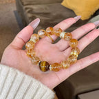 Woman hand holding natural citrine tiger eye abundance manifestation bracelet gold crown spacers white knit sweater background Taoist KaiGuang prosperity manifestation