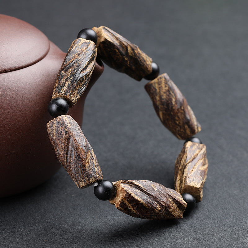 Side view of aged agarwood meditation bracelet with raw irregular chunks and black obsidian beads beside purple clay teapot Taoist KaiGuang protection