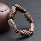 Side view of aged agarwood meditation bracelet with raw irregular chunks and black obsidian beads beside purple clay teapot Taoist KaiGuang protection
