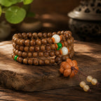 TAIJIAURA consecrated agarwood mala 108 beads stacked on natural stone with jade green white accent beads carved flower pendant bronze incense burner green leaves warm light spiritual anchor clarity energetic fortification