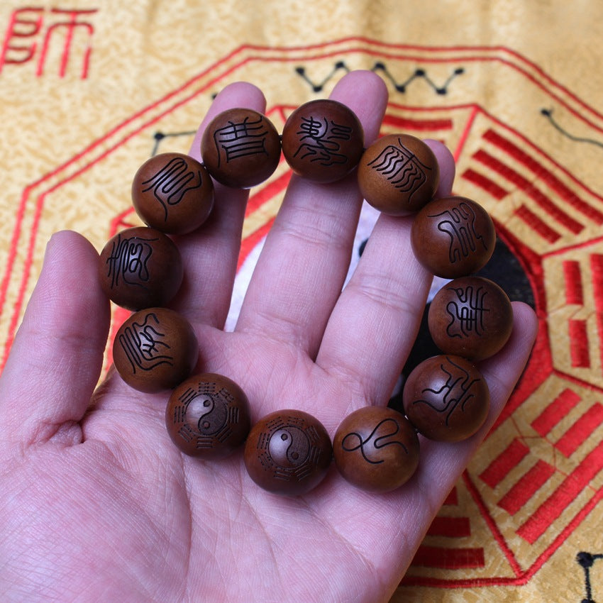 The complete aged dark wood Ten Character Heavenly Scripture bracelet with 12 large beads, lies flat on a light wood grain surface near a black Chinese stand, designed for neutralizing negative energy.