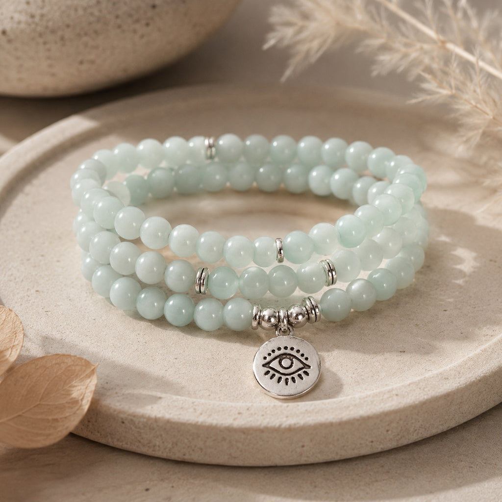 Amazonite 108 bead mala bracelet triple wrap with eye of truth silver pendant on beige ceramic plate natural light pampas grass background meditation gemstone jewelry