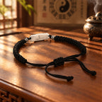 Black cord Taoist talisman bracelet with silver luck charm resting on a wooden tea table