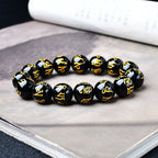 Black obsidian mantra bracelet with vivid gold ancient script carving detail photographed on open book background
