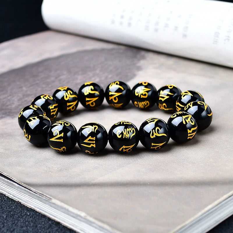 Black obsidian mantra bracelet with vivid gold ancient script carving detail photographed on open book background