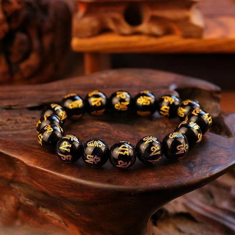  Black obsidian bracelet with gold mantra carvings resting in dark wood bowl, Taoist KaiGuang consecrated protection jewelry
