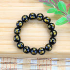 Black obsidian gold mantra bracelet on bamboo surface with green leaves natural lifestyle shot Taoist protection jewelry