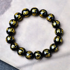 Black obsidian six syllable mantra bracelet laid flat on white marble showing complete gold carved script circle