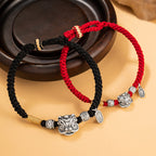 Black and red braided cord couple love protection bracelets displayed together on warm yellow background with dark wood tray showing silver lion head charms and rune beads