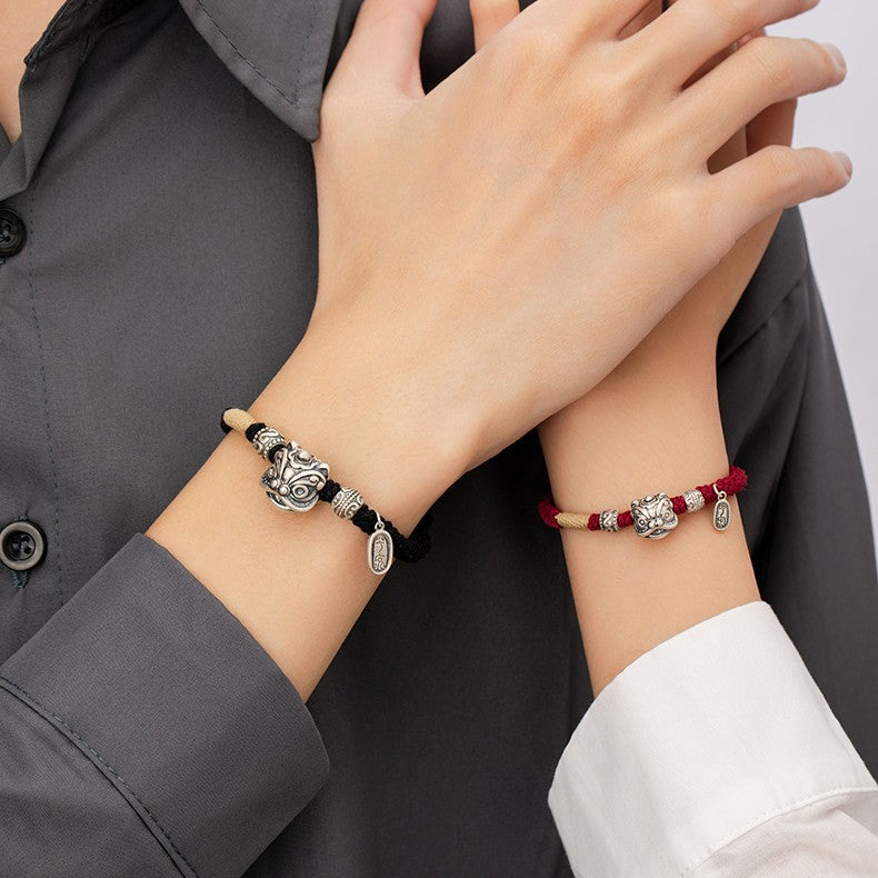 Man and woman wearing matching love protection bracelets with silver lion head charms black cord for men red cord for women hands together showing Taoist KaiGuang couple soul bond jewelry
