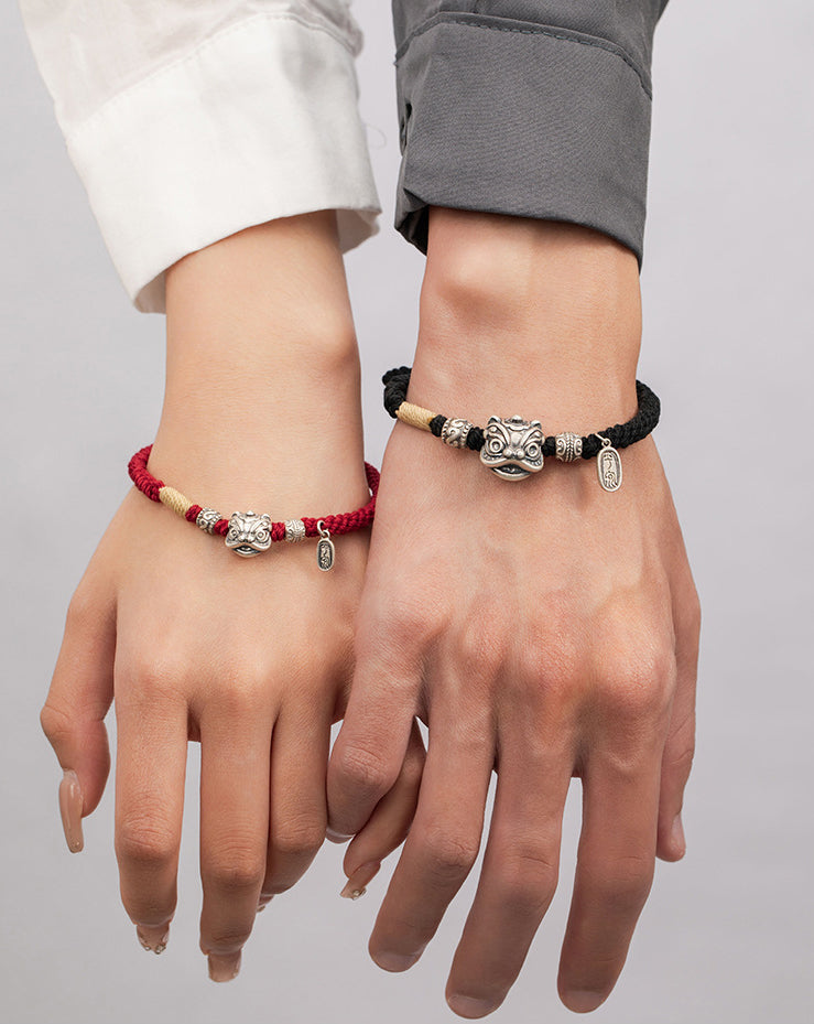 Woman wearing red cord and man wearing black cord love protection bracelets side by side hands facing up showing silver lion head charms Taoist KaiGuang faithful bond couple jewelry