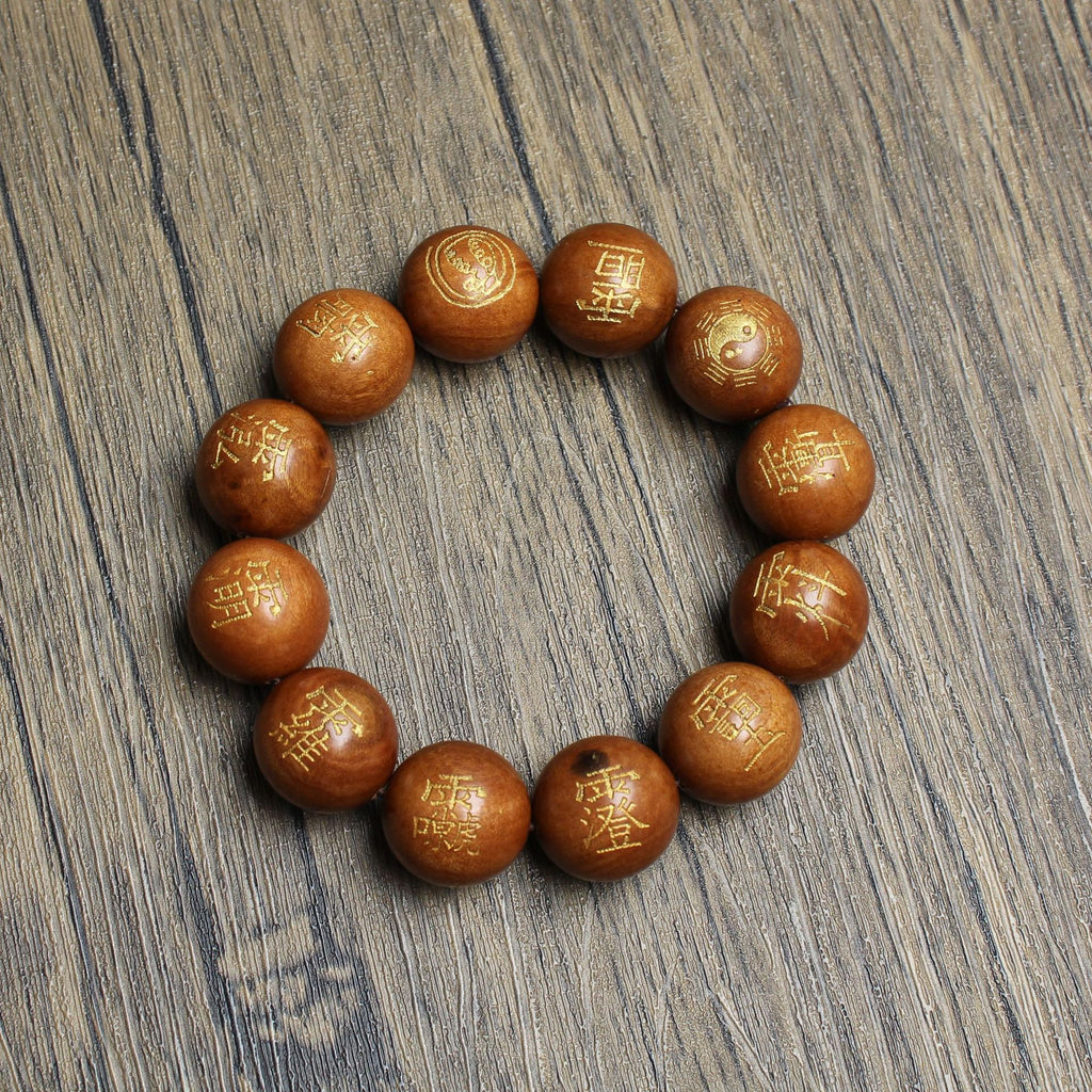 A functional energy tool for Feng Shui protection: The complete gold-painted thunderstruck wood bracelet with Five Thunders Talisman scripts lies flat on a light wood grain surface near a traditional black Chinese stand, designed to neutralize Sha Chi.