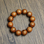 A functional energy tool for Feng Shui protection: The complete gold-painted thunderstruck wood bracelet with Five Thunders Talisman scripts lies flat on a light wood grain surface near a traditional black Chinese stand, designed to neutralize Sha Chi.