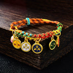 Five Gods of Wealth Taoist KaiGuang bracelet five-color braided rope gold enamel medallions on dark wood surface