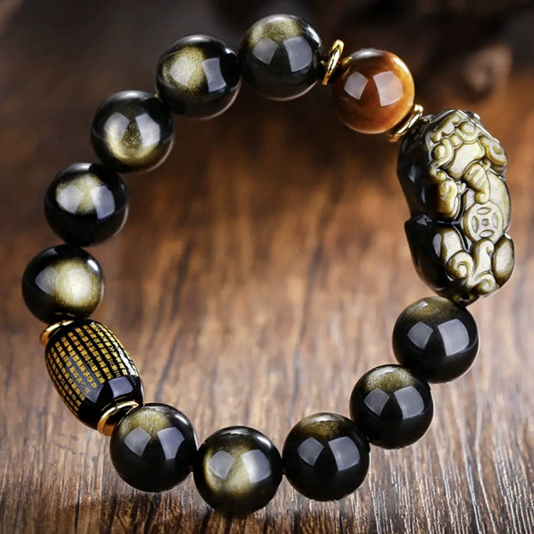 Gold obsidian Pixiu wealth attraction bracelet with tiger eye and engraved scripture barrel on wooden surface
