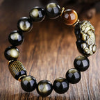Gold obsidian Pixiu wealth attraction bracelet with tiger eye and engraved scripture barrel on wooden surface