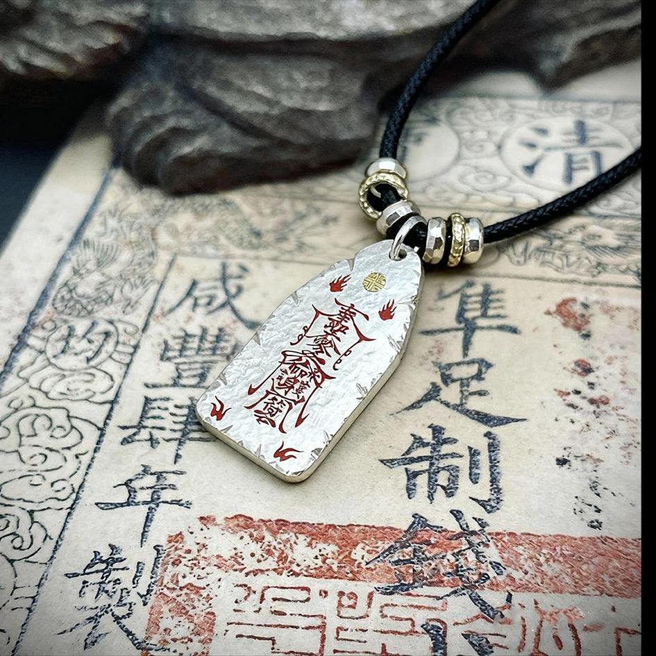 Hand-hammered sterling silver protection talisman with red cinnabar-filled Taoist symbols on a vintage background.