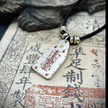 Hand-hammered sterling silver protection talisman with red cinnabar-filled Taoist symbols on a vintage background.