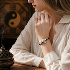 Woman in white shirt wearing jade peace buckle protection bracelet on wrist hands clasped silver twisted rope black yin yang beads yin yang bagua backdrop bronze incense burner smoke Taoist KaiGuang evil warding yin yang balance amulet