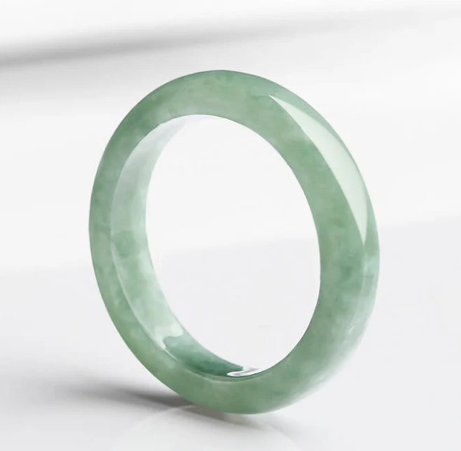 Natural jadeite evil ward ring tilted on white background showing soft green tone with natural grey-green veining
