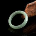  Natural jadeite KaiGuang ring resting against dark driftwood showing light green translucent surface with reflection