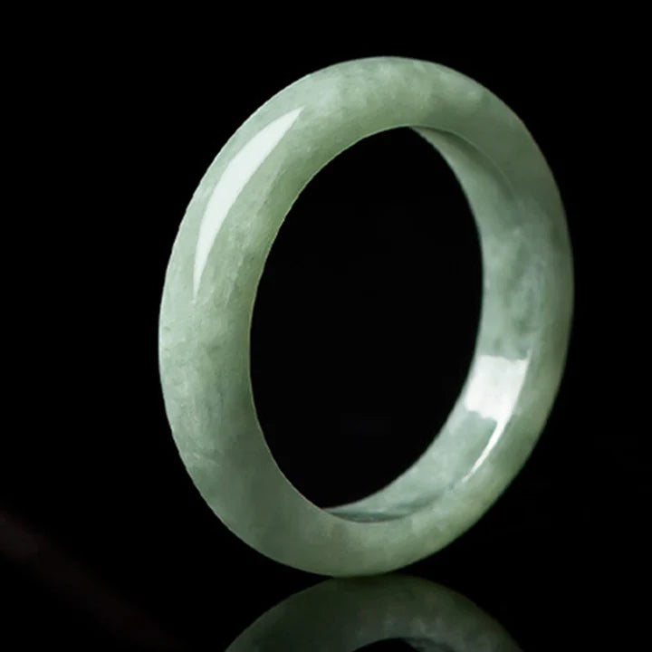 Jadeite wealth ring standing upright on black background at angle showing natural green grain and polished gloss