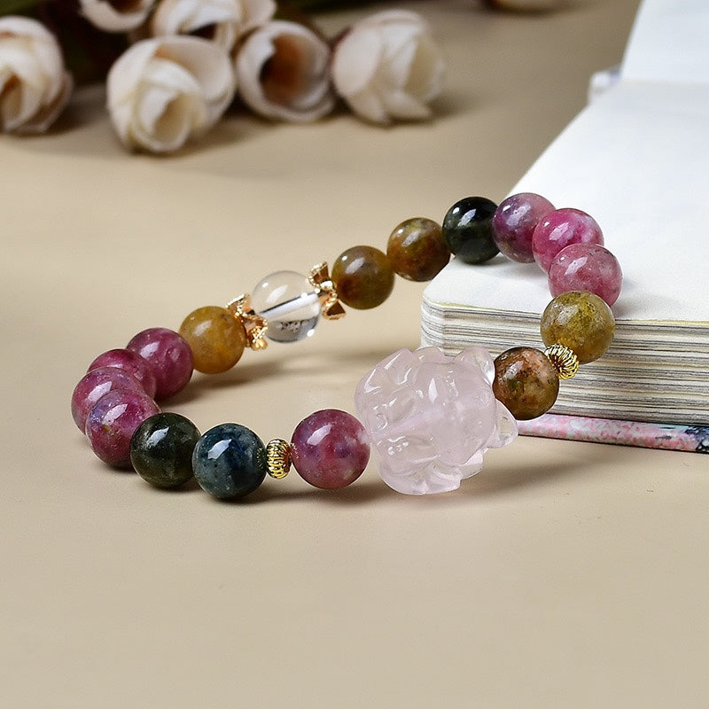 Natural rainbow tourmaline and rose quartz nine-tail fox crystal love attraction bracelet with clear quartz ball gold spacers beside white flowers and book Taoist KaiGuang charm healing