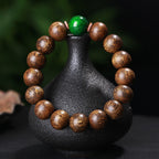 Black oil agarwood luck change bracelet with green jade bead displayed on black vase prop showing tiger stripe wood grain texture Taoist KaiGuang evil ward protection spiritual jewelry