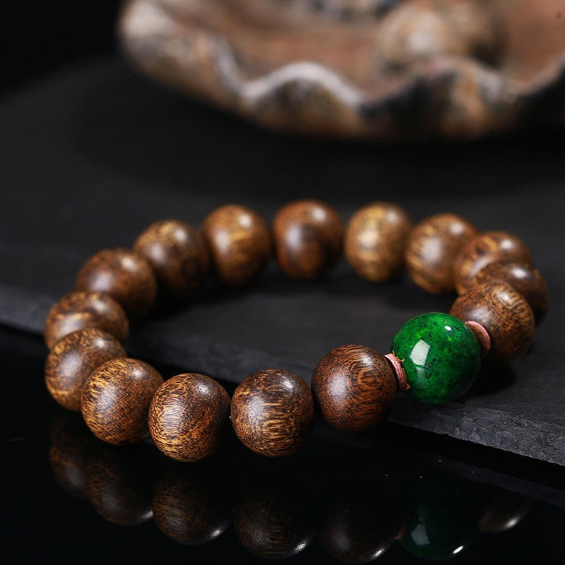 Close-up of black oil agarwood luck change bracelet showing green jade bead and copper spacer detail on dark stone with shell prop Taoist KaiGuang evil ward protection spiritual bracelet
