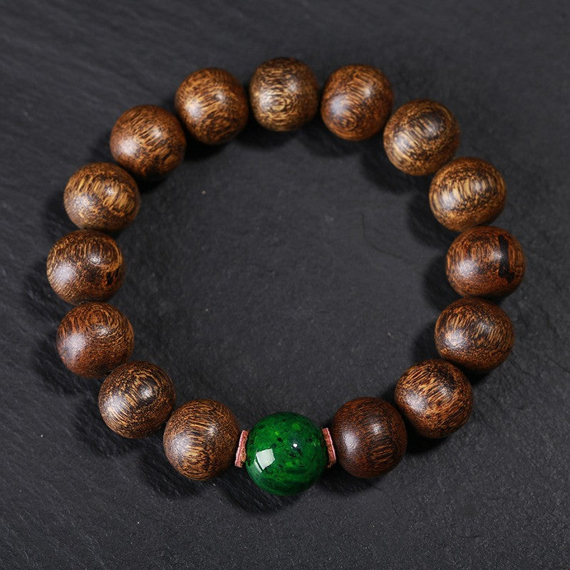 Black oil agarwood luck change bracelet full circle view on gray stone background showing natural wood grain texture with green jade center bead Taoist KaiGuang evil ward protection