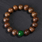 Black oil agarwood luck change bracelet full circle view on gray stone background showing natural wood grain texture with green jade center bead Taoist KaiGuang evil ward protection